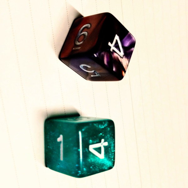 A photograph of two dice on a white page. One dice is violet. The other is green.